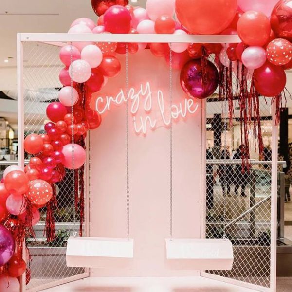 Crazy in Love neon sign wall mounted on a department store display with balloons and lover's swings - photo from Custom Neon (formerly Neon Collective)
