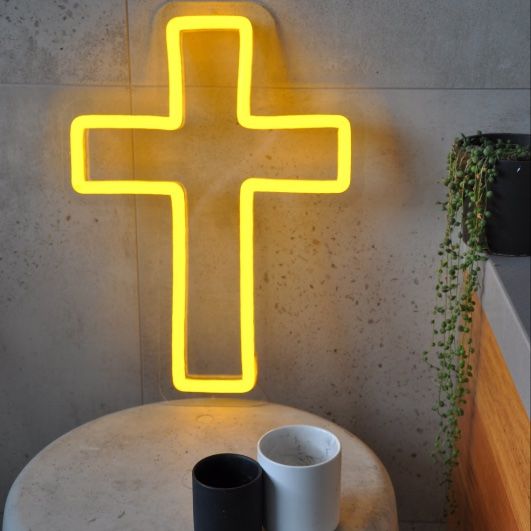 LED neon cross shown illuminated in yellow, on a side table - from Custom Neon by Neon Collective