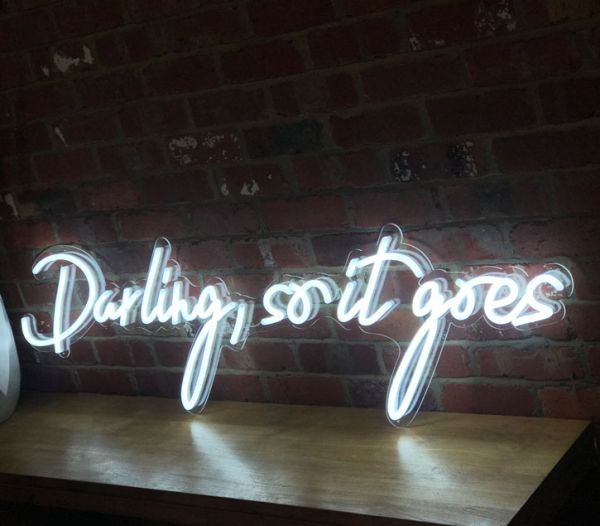Beautiful cursive neon word sign * Darling, so it goes * shown against exposed brick wall
 - photo from CustomNeon.co.uk