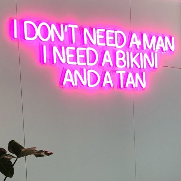 Pink neon sign featuring the words I Don't Need a Man I Need a Bikini and a Tan shown turned on against a white wall - from Custom Neon®