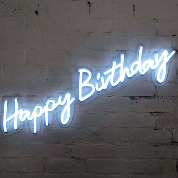 * Happy Birthday * is a lightweight, portable neon sign in modern cursive font, shown against a brick wall. Photo from CustomNeon.co.uk

