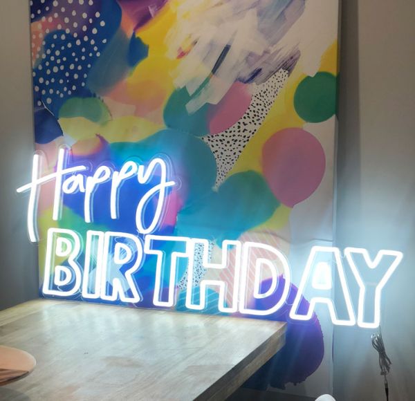 Happy Birthday is a double line LED neon word sign in two fonts on clear acrylic backboard that is cut around the shape. Photo from Custom Neon (formerly Neon Collective)
