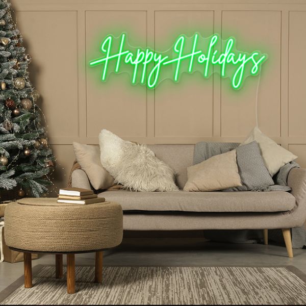 CUSTOM NEON® Happy Holidays green light sign wall mounted in a living room next to a decorated Christmas tree.