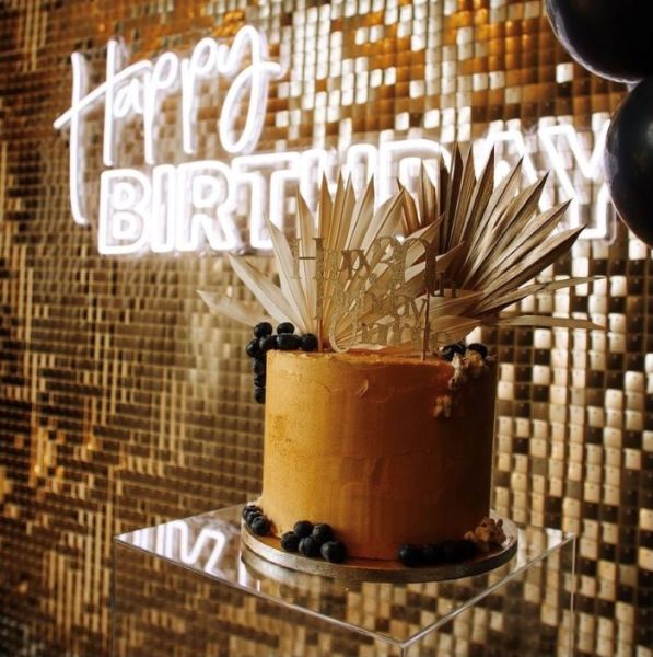 Custom Neon® Happy Birthday sign in white LED neon flex on a golden shimmer wall behind a birthday cake  @raspberrycraftsandevents.