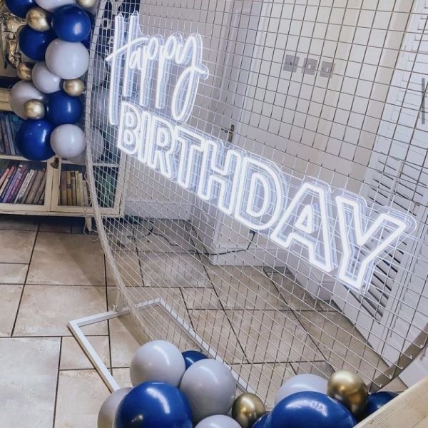 Happy birthday neon lettering sign shining between balloons. Stock Photo