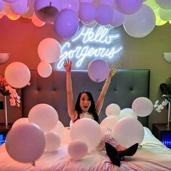 Hello Gorgeous LED neon light up sign shown above a bed with balloons - photo from CustomNeon.co.uk