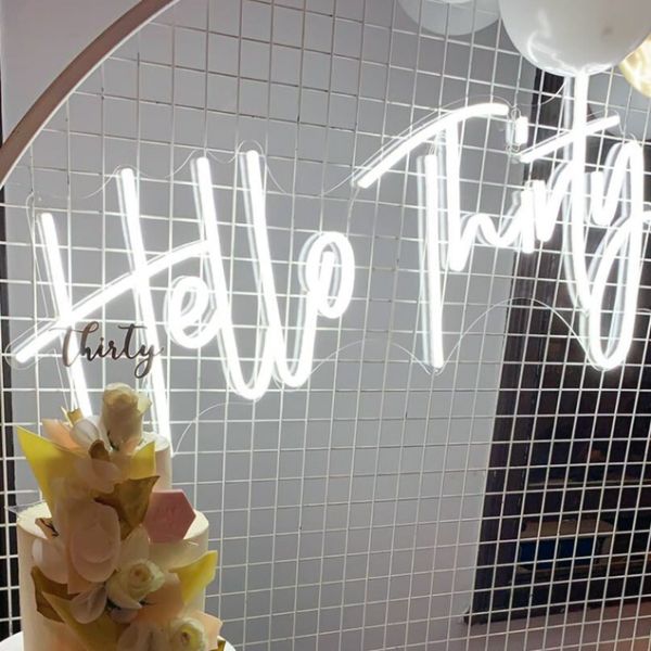 Hello Thirty Light Up Birthday Sign shown in white on mesh in front of the birthday cake - photo from CustomNeon.com