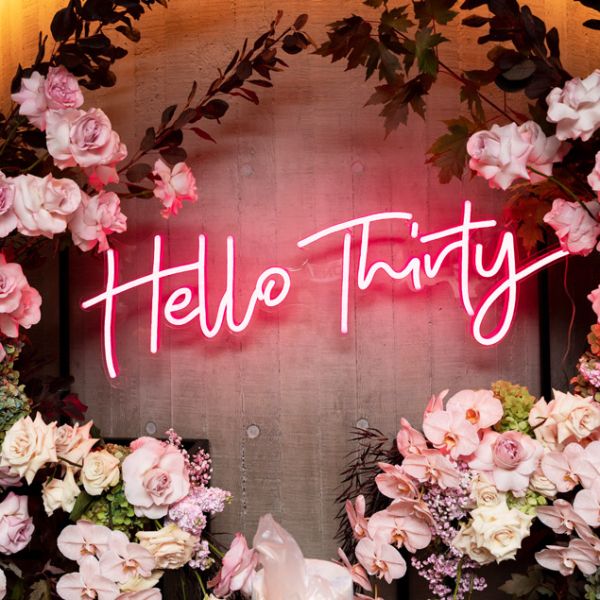 Hello Thirty Light Up Birthday Sign in pink surrounded by floral decorations - photo from CustomNeon.com