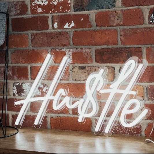 Hustle Neon Sign shown on an exposed brick wall  - photo from CustomNeon.com 