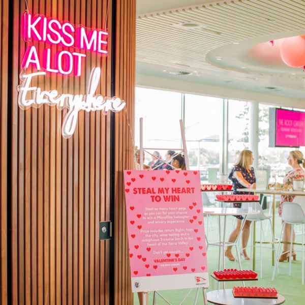 Kiss Me A Lot Everywhere LED Neon Sign shown hung from the entrance to a Valentine's Day event - photo CustomNeon.com