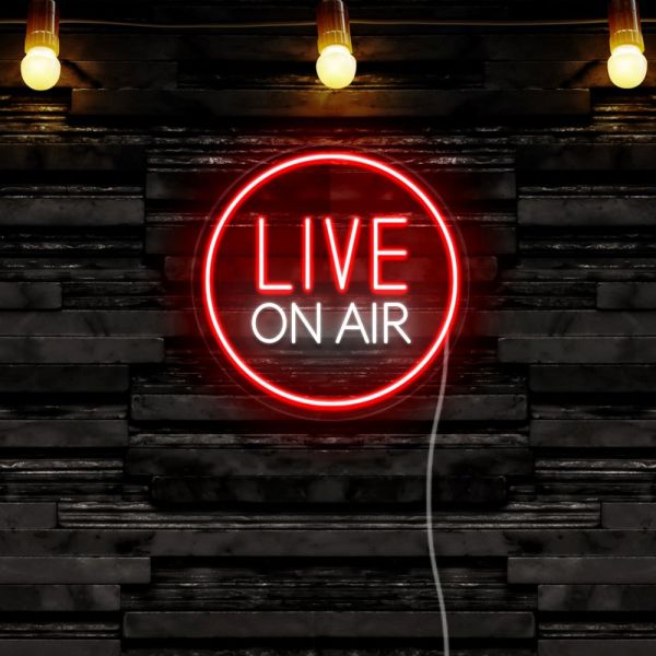 CUSTOM NEON® Live on Air studio sign shown in red and white mounted on a black stone wall with spotlights overhead