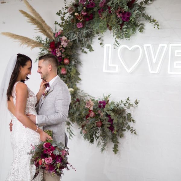 LOVE Light Up Sign with a heart - photo of Custom Neon's founders, Jake and Jess, at their wedding with the LOVE sign mounted on the photo wall.  - photo from Custom Neon by Neon Collective