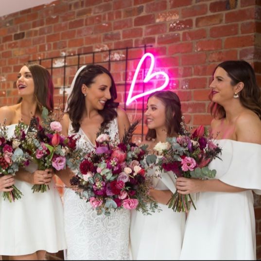 LED neon heart light for wedding decor shown wall mounted in pink with Custom Neon's founder, Jess Munday, and her bridesmaids