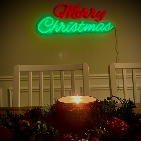 Red & green Merry Christmas neon light by CUSTOM NEON® wall mounted with a festive candle and holly centrepiece in the foreground.