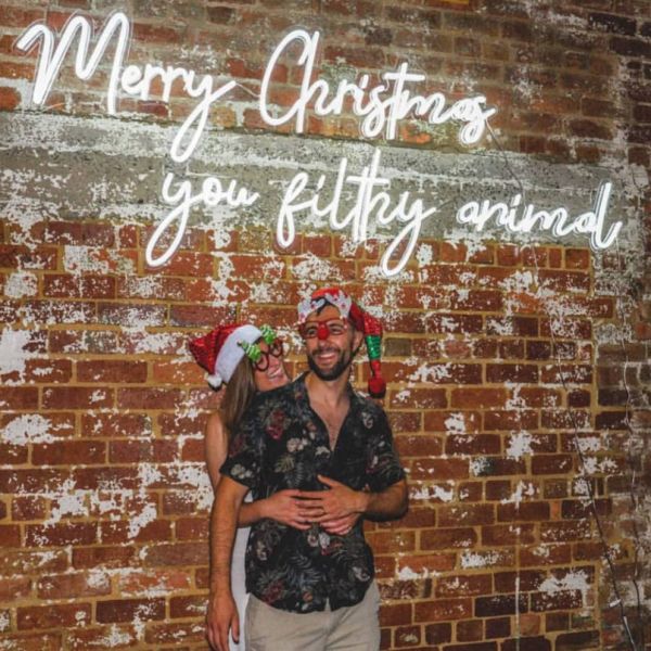 Merry Christmas You Filthy Animal LED Neon Sign shown on an exposed brick wall at a Xmas party - photo from Custom Neon by Neon Collective