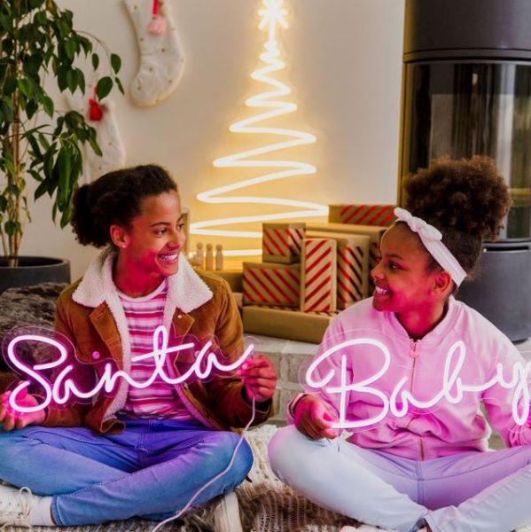 Santa Baby pink light-up sign shown in a living room with other Christmas decorations - by CUSTOM NEON®