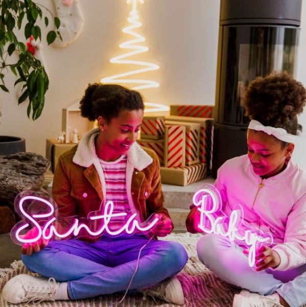 Santa Baby pink light-up sign shown in a living room with other Christmas decorations - by CUSTOM NEON®