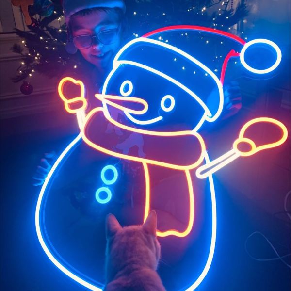 Custom Neon® snowman in bright white and warm white LED neon flex held by a child in front of a Christmas tree
