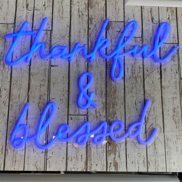 Thankful & Blessed blue neon sign with blue jacket shown on wooden wall - made by @customneon for @9gramscafe 