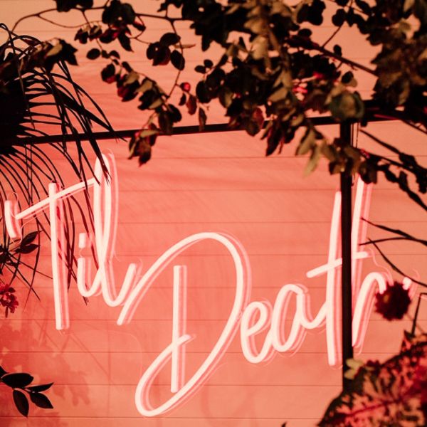 Til Death LED neon sign shown hanging from a frame at a wedding - photo from CustomNeon.co.uk