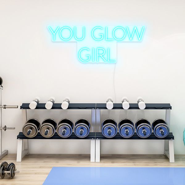 You Glow Girl light blue CUSTOM NEON® sign shown on a white wall above weights in a gym