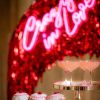Custom Neon® hot pink LED neon sign on a red background with wedding donuts and cocktails in the foreground.