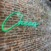 Cheers Neon Bar Sign in green on a brick wall @margaritascantina made by Custom Neon®