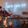 Love You XO LED neon light shown mounted on a brick wall behind the sweets table at an event - photo CustomNeon.co.uk