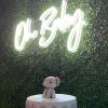 Oh Baby white LED neon sign shown on a green wall above a baby shower cake @CustomNeon.uk