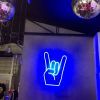 Rock On Emoji LED Neon Sign shown in blue, wall mounted in a fashion store - photo from Custom Neon by Neon Collective