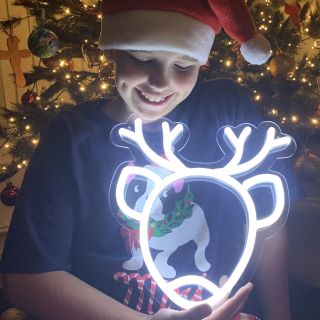 Custom Neon® white LED neon reindeer face held by a child in front of a Christmas tree