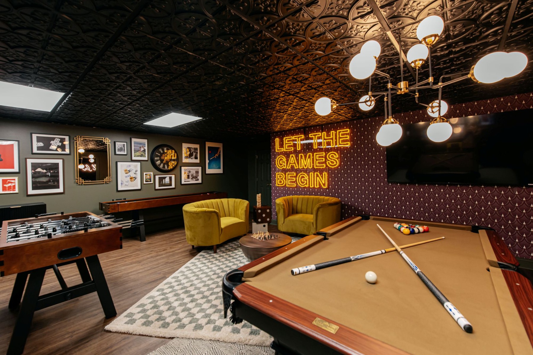 Let the Games Begin large dark yellow on a dark wall Custom Neon® sign in the games room of an Airbnb home designed by Somerled