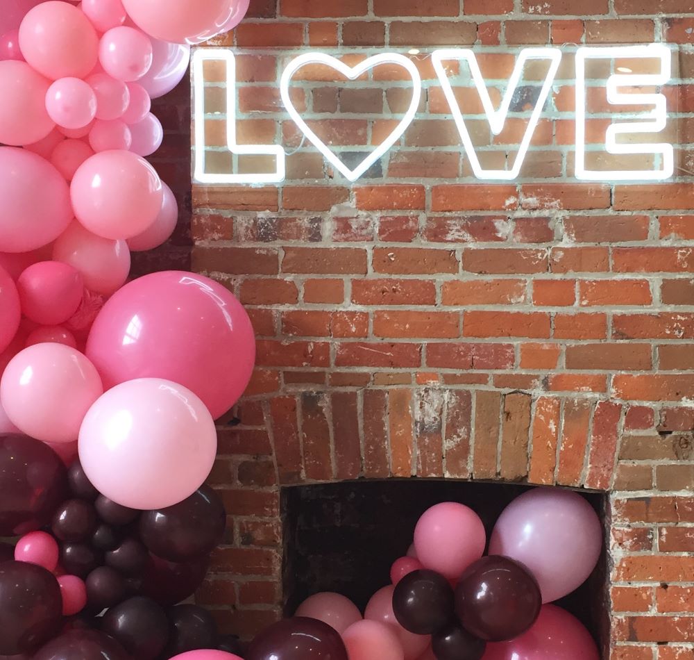 Custom Neon® white LOVE sign with heart mounted on brick fireplace with balloon arch