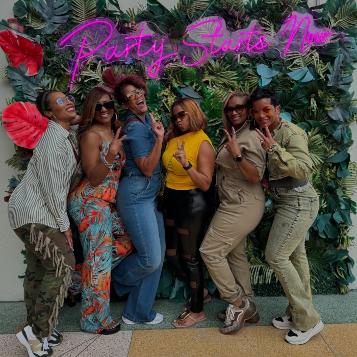 Party Starts Now pink Custom Neon® sign on a plant wall behind people taking a selfie @clevelander